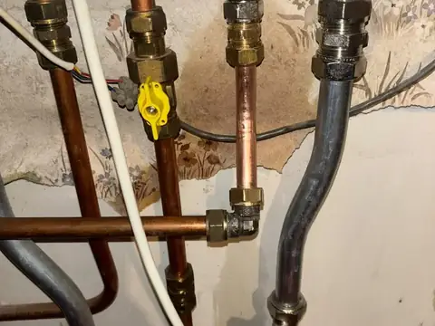 Koperen leidingen met afsluiters en gasleiding onder een cv-ketel