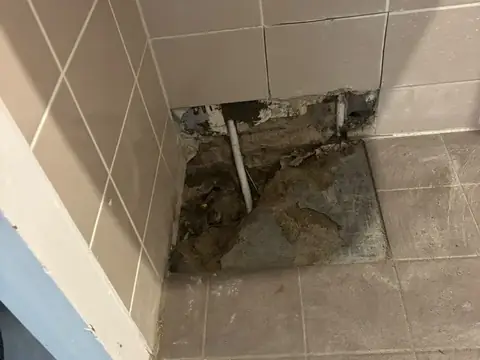 Opengemaakte vloerhoek met blootgelegde leiding in een doucheruimte