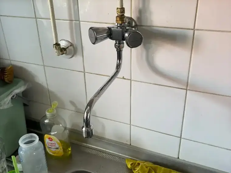 Keukenkraan boven een spoelbak met leiding langs de wand