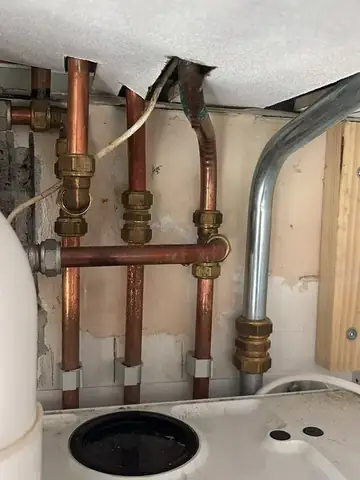 Koperen leidingwerk met koppelingen boven een sanitairaansluiting