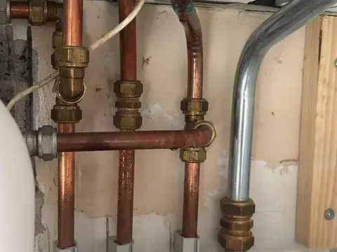 Koperen leidingwerk met koppelingen boven een sanitairaansluiting